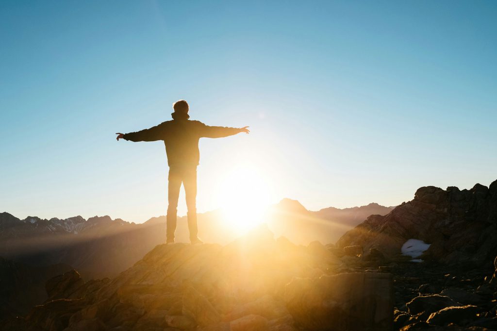man standing with arms outstretched on a mountain at sunrise